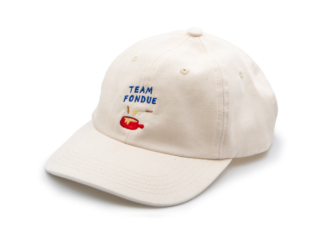 Nature farbenes Dad Cap auf weissem Hintergrund mit blauem gesticktem Schriftzug "Team Fondue" sowie rotem gesticktem Fondue Caquelon.
