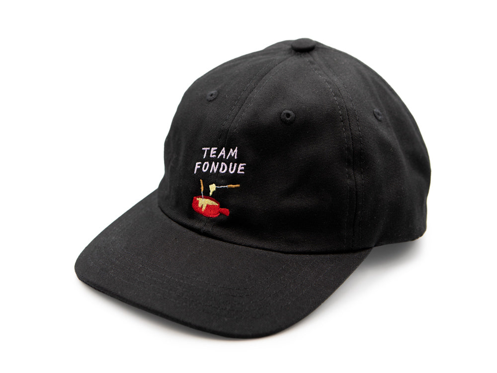 Schwarzes Dad Cap auf weissem Hintergrund mit blauem gesticktem Schriftzug "Team Fondue" sowie rotem gesticktem Fondue Caquelon.