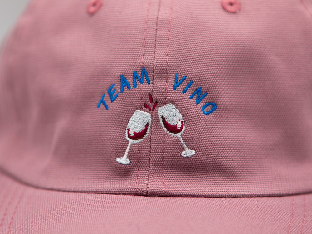 Detailaufnahme einer Stickerei mit dem Schriftzug Team Vino und zwei gestickten Weingläsern auf rosa farbenem Stoff