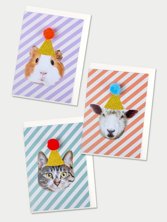 Drei Postkarten, eine lila-weiss schräg gestreift mit Meerschweinchen mit goldenem Hut und orangem Pompon, eine eine türkis-weiss schräg gestreift mit Katze mit goldenem Hut und rotem Pompon und eine eine orange-weiss schräg gestreift mit Schaf mit goldenem Hut und grünem Pompon auf beigem Hintergrund