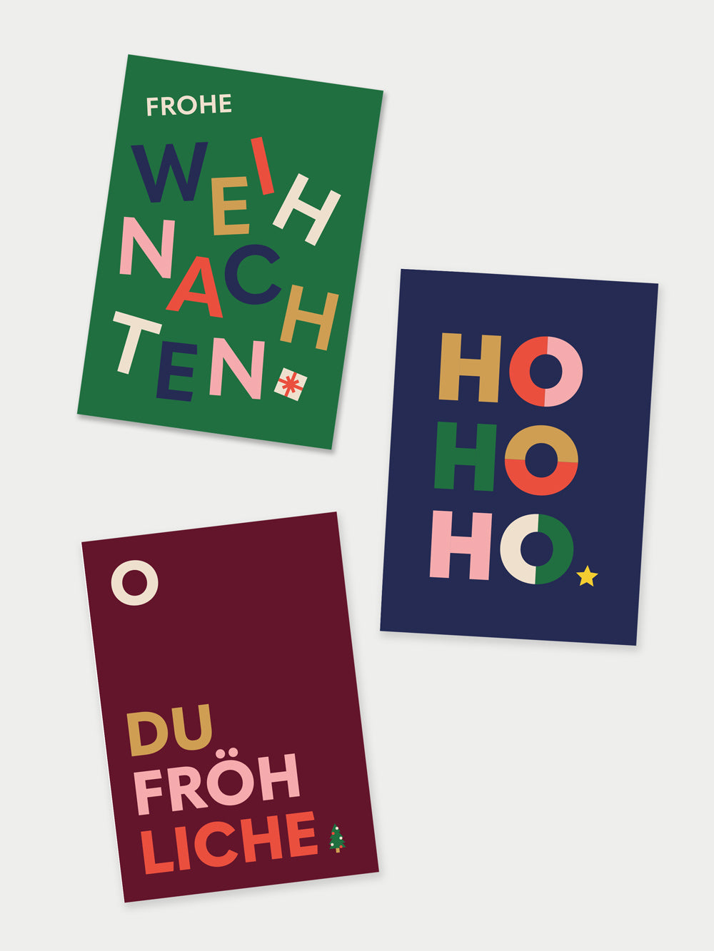 Drei Postkarten, eine Grün mit farbigem Schriftzug Frohe Weihnachten, eine dunkelblau mit Schriftzug HOHOHO, eine dunkelrot mit dem Schriftzug O du Fröhliche
