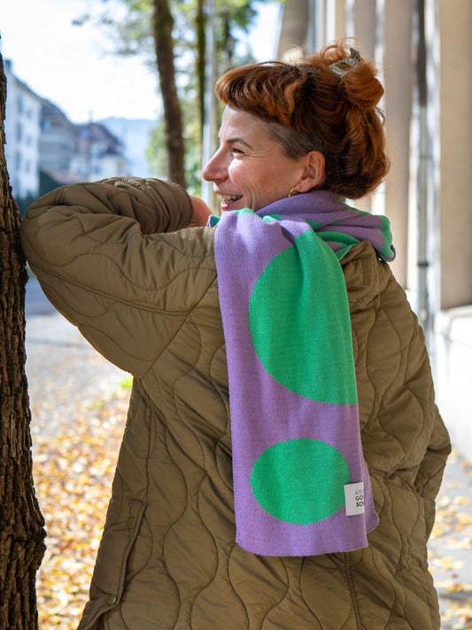 Frau mit beiger Steppjacke und orangen Haaren trägt mint lila gepunkteten Jaquard Schal