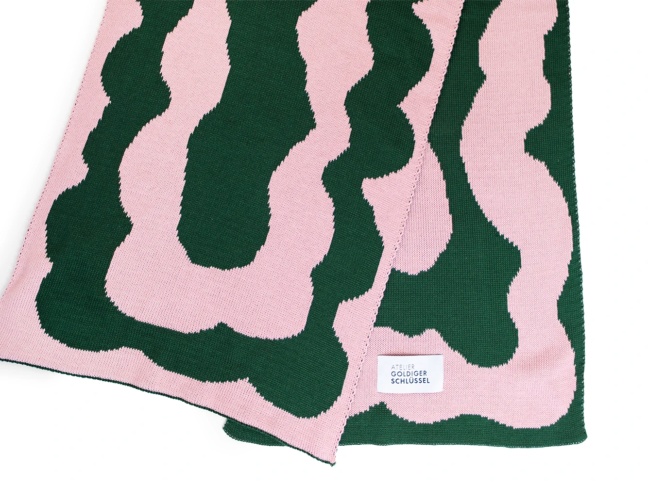 Detailansicht eines Grün rosa gemusterten Schals aus Bio-Baumwolle vom Label von Atelier Goldiger Schlüssel auf weissem Untergrund.