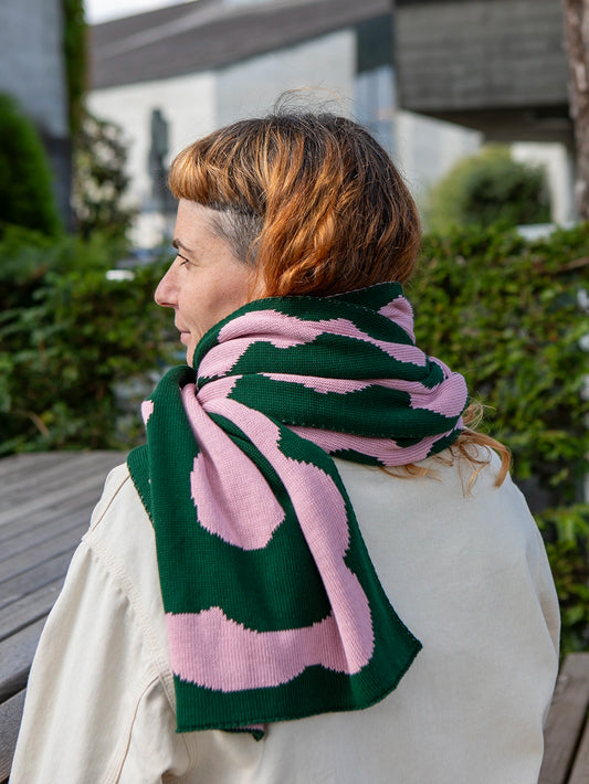 Oberkörper einer Frau mit orangen Haaren von hinten. Die Frau trägt einen rosa grün gemusterten Strickschal.