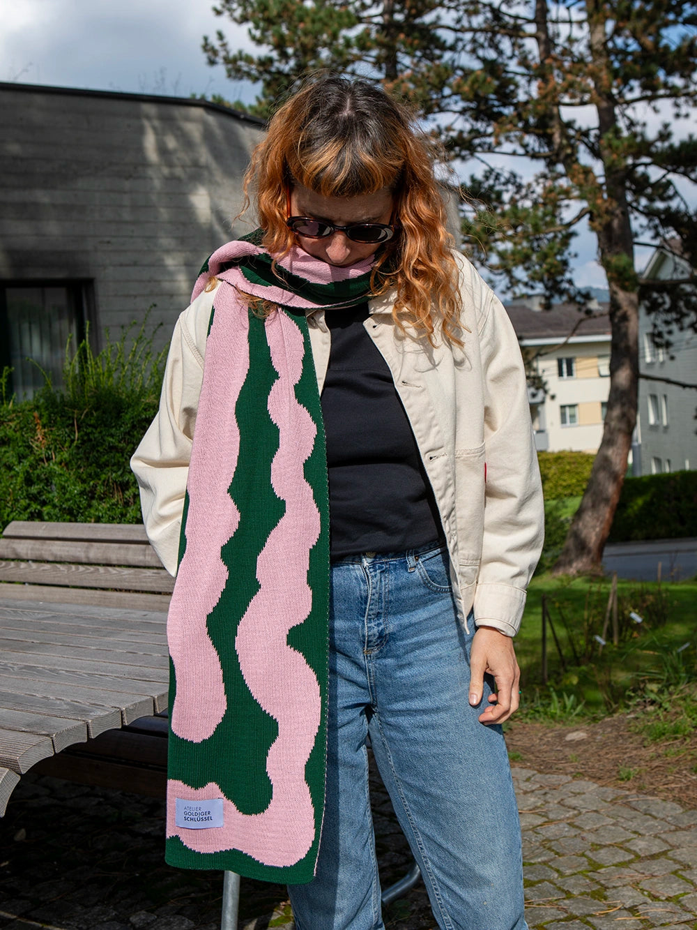 Oberkörper einer Frau mit orangen Haaren die eine Jack in offwhite und einen rosa grün gemusterten Strickschal trägt