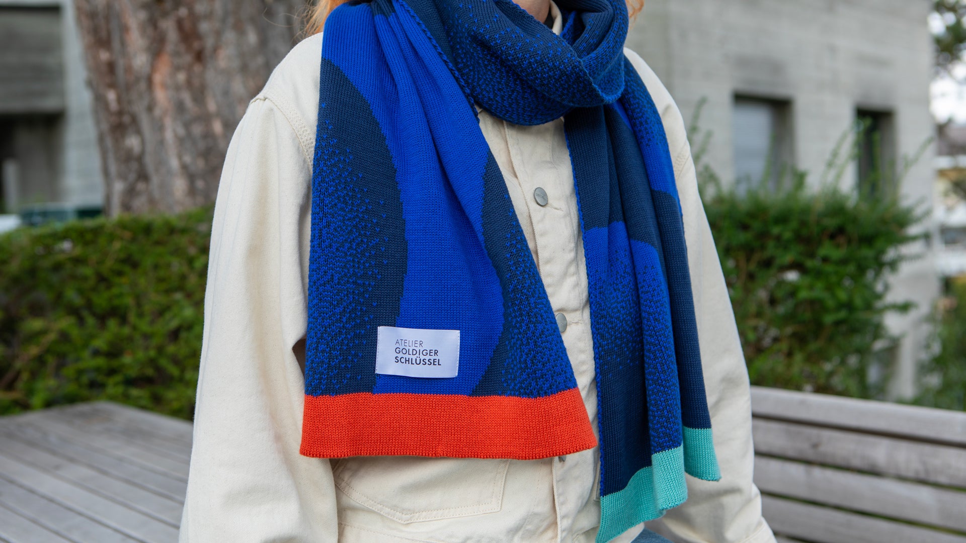 Oberkörper mit Carhartt Jacke in off white di einen Jaquard Schal in zwei unterschiedlichen Blau tönen und mit bunten Enden trägt.