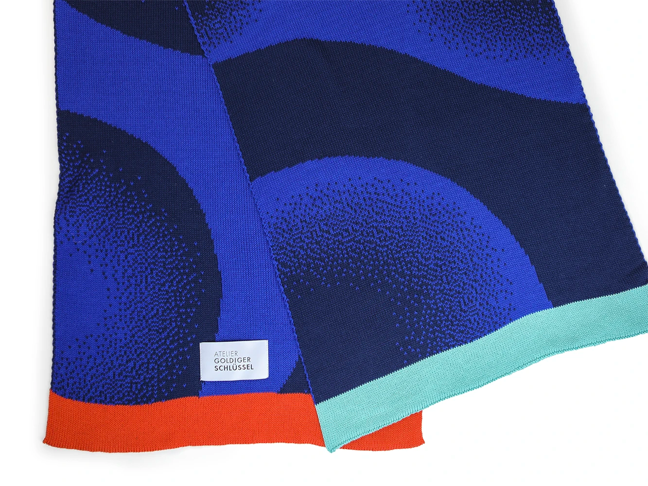 Detailansicht der Vor- und Rückseite eines blau gemusterten Schals mit zwei farbigen Enden in rot-orange und mint.