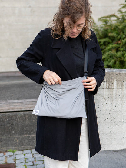 Frau mit blonden Locken und einer schwarzen Jacke trägt eine reflektierende Umhängetasche mit dem Label «Atelier Goldiger Schlüssel».