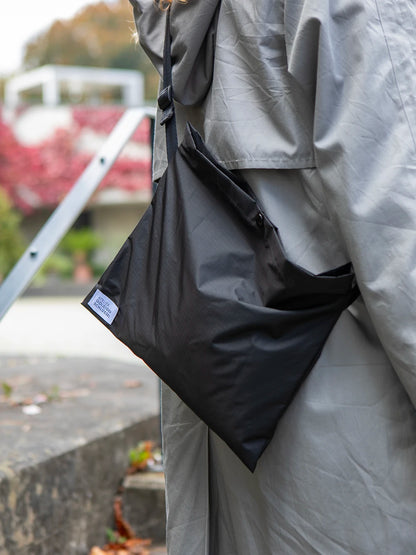 Ausschnitt eines Oberkörpers mit hellgrauer Jacke, welche eine schwarze Umhängetasche mit dem weissen Label «Atelier Goldiger Schlüssel» trägt.