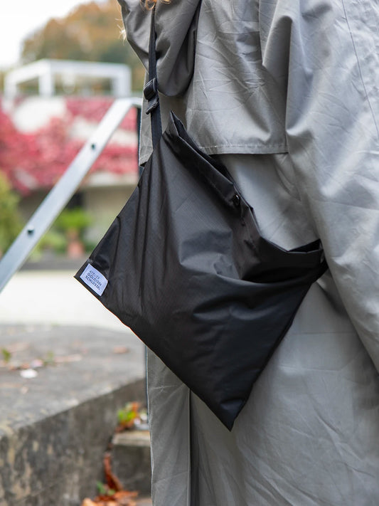 Ausschnitt eines Oberkörpers mit hellgrauer Jacke, welche eine schwarze Umhängetasche mit dem weissen Label «Atelier Goldiger Schlüssel» trägt.