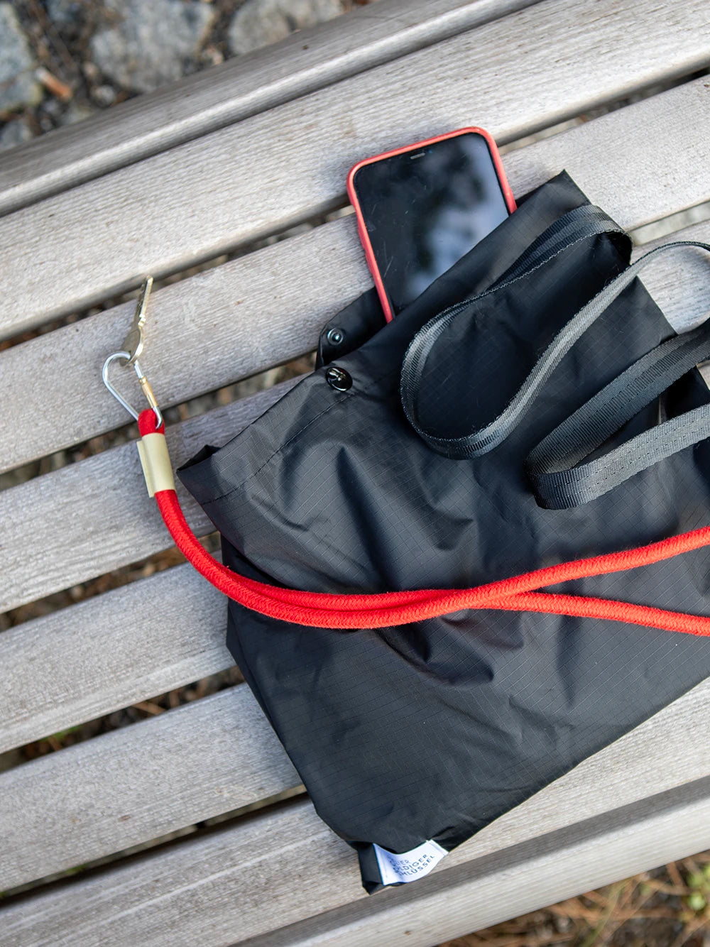 Aufsicht einer schwarzen Tasche auf verbleichten Holzlatten mit einem roten Telefon und einem roten Schlüsselband.