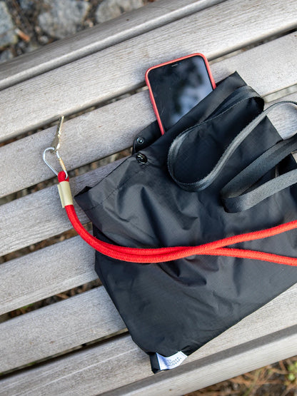 Aufsicht einer schwarzen Tasche auf verbleichten Holzlatten mit einem roten Telefon und einem roten Schlüsselband.